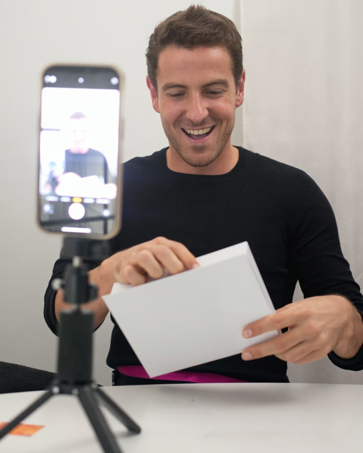Mann packt ein Paket aus, ein Smartphone auf dem Stativ filmt mit