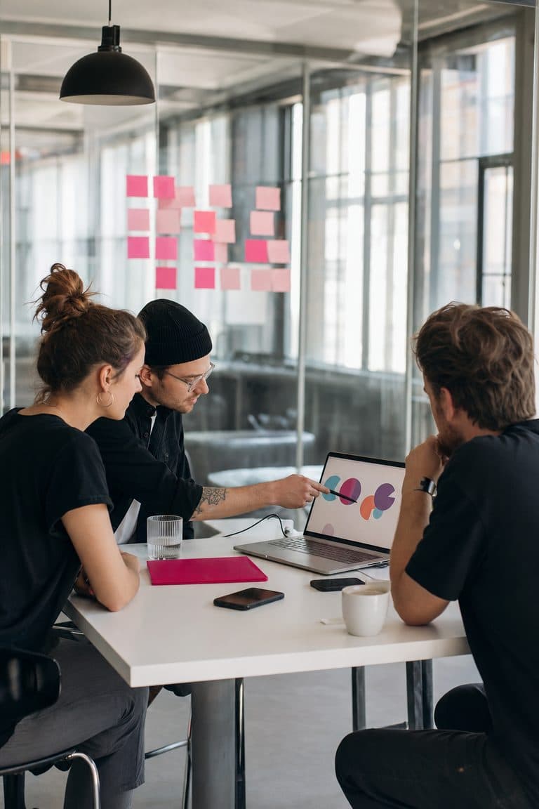 Strategie-Workshop: drei Menschen am Tisch mit Diagrammen am Laptop