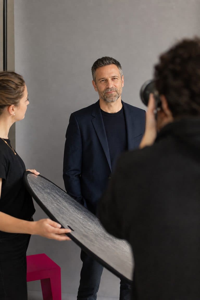 Porträt-Shooting: Mann im Blazer vor grauem Hintergrund, Assistentin hält einen Reflektor