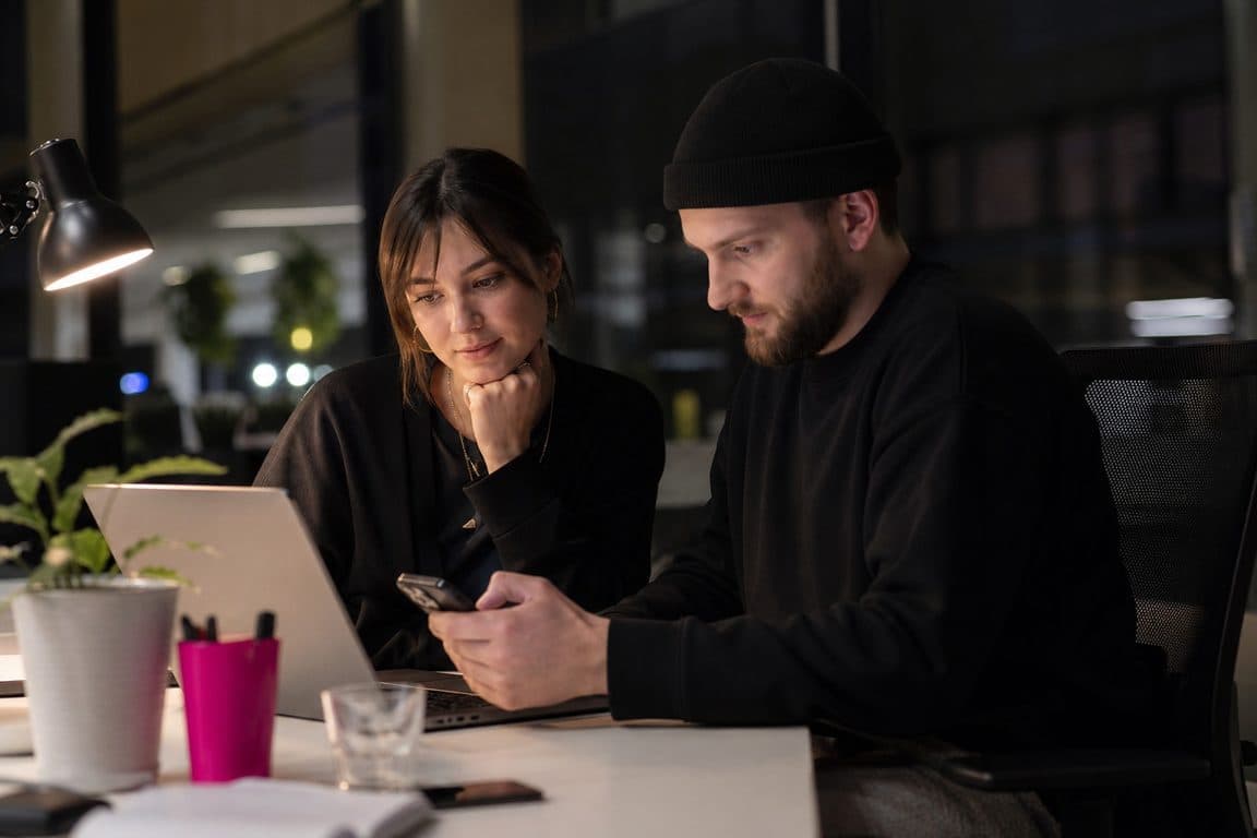 Zwei Kolleginnen sortieren am Abend eingehende Kommentare an Laptop und Handy