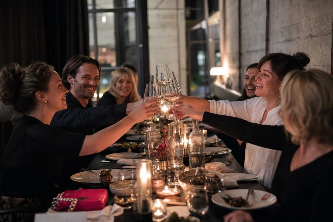 Gäste stoßen an einer langen Tafel im Kerzenlicht an