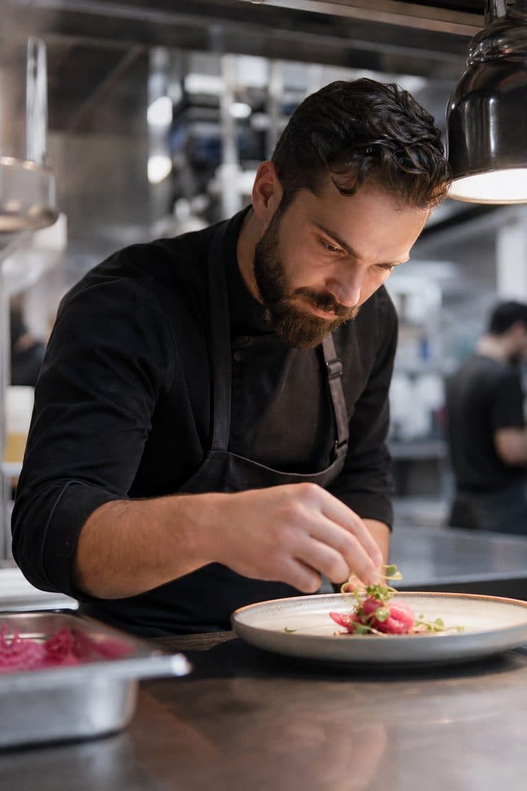 Koch richtet am Pass einer Restaurantküche einen Teller an