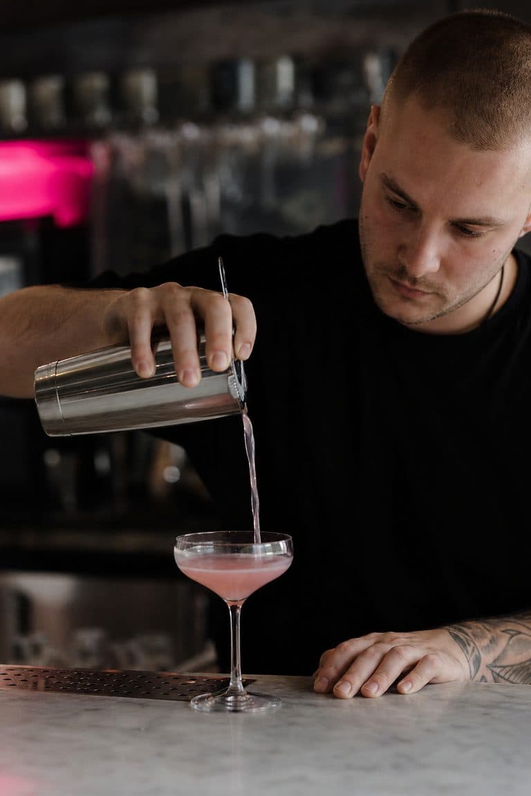 Barkeeperin gießt einen pinken Cocktail ein