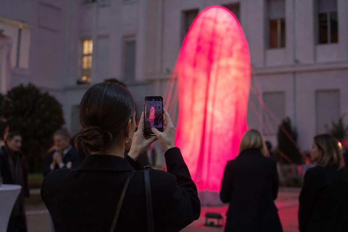 Gäste fotografieren am Abend eine pinke Lichtinstallation im Innenhof