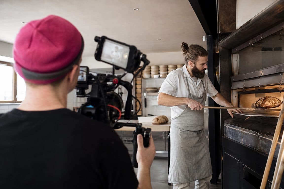 Kamerafrau filmt einen Bäcker, der Brot aus dem Ofen holt
