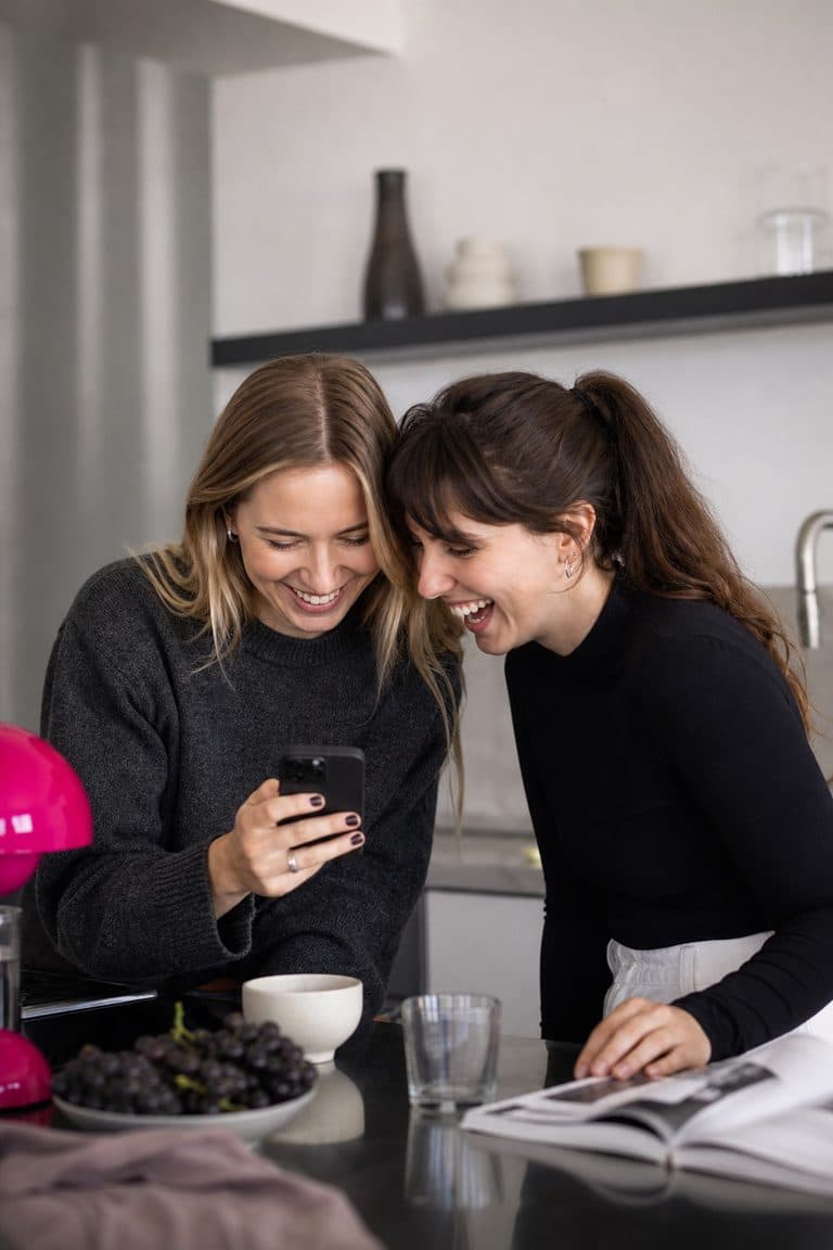 Zwei Freundinnen schauen an der Küchentheke lachend aufs Handy