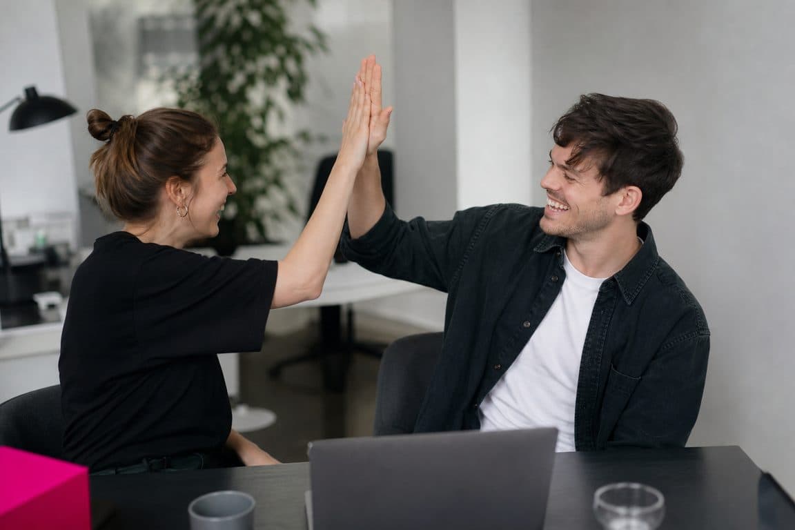 Zwei Kollegen klatschen sich am Schreibtisch nach guten Ergebnissen ab