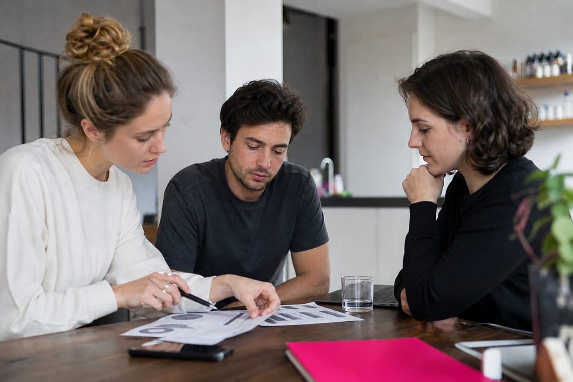 Kleines Team geht am Küchentisch ausgedruckte Budgetpläne durch