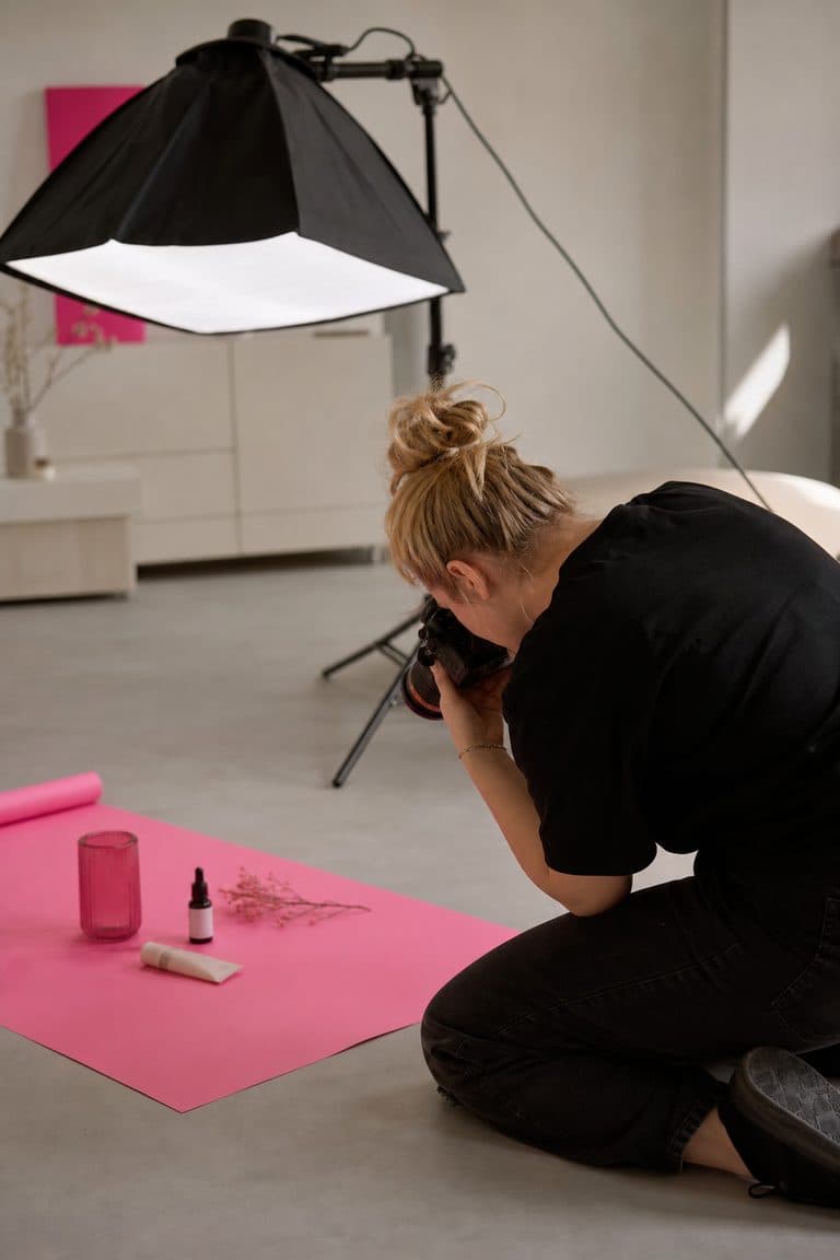 Fotograf kniet am Boden und fotografiert ein Produkt-Flatlay auf pinkem Papier