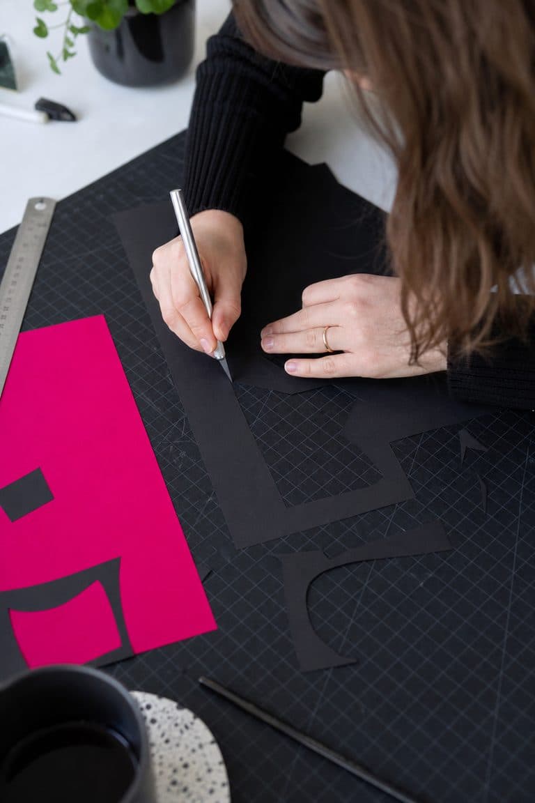 Designerin schneidet pinke und schwarze Papierformen auf der Schneidematte