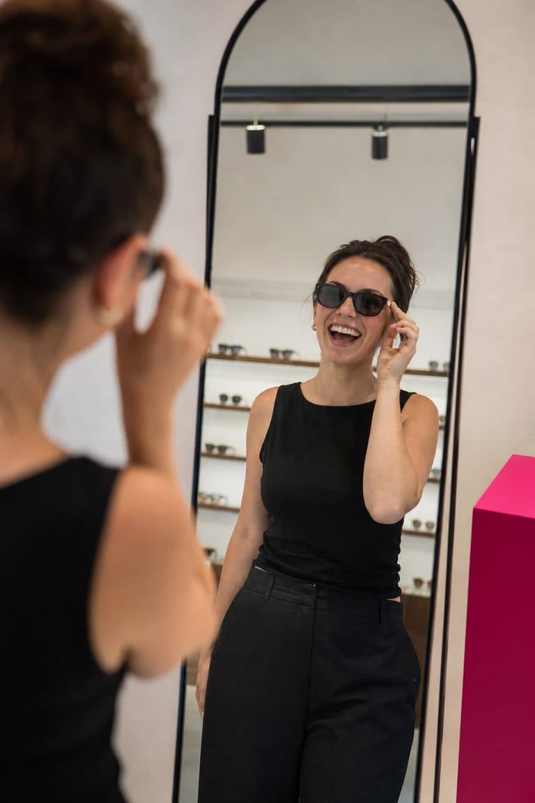 Kundin probiert lachend eine Sonnenbrille vor dem Spiegel