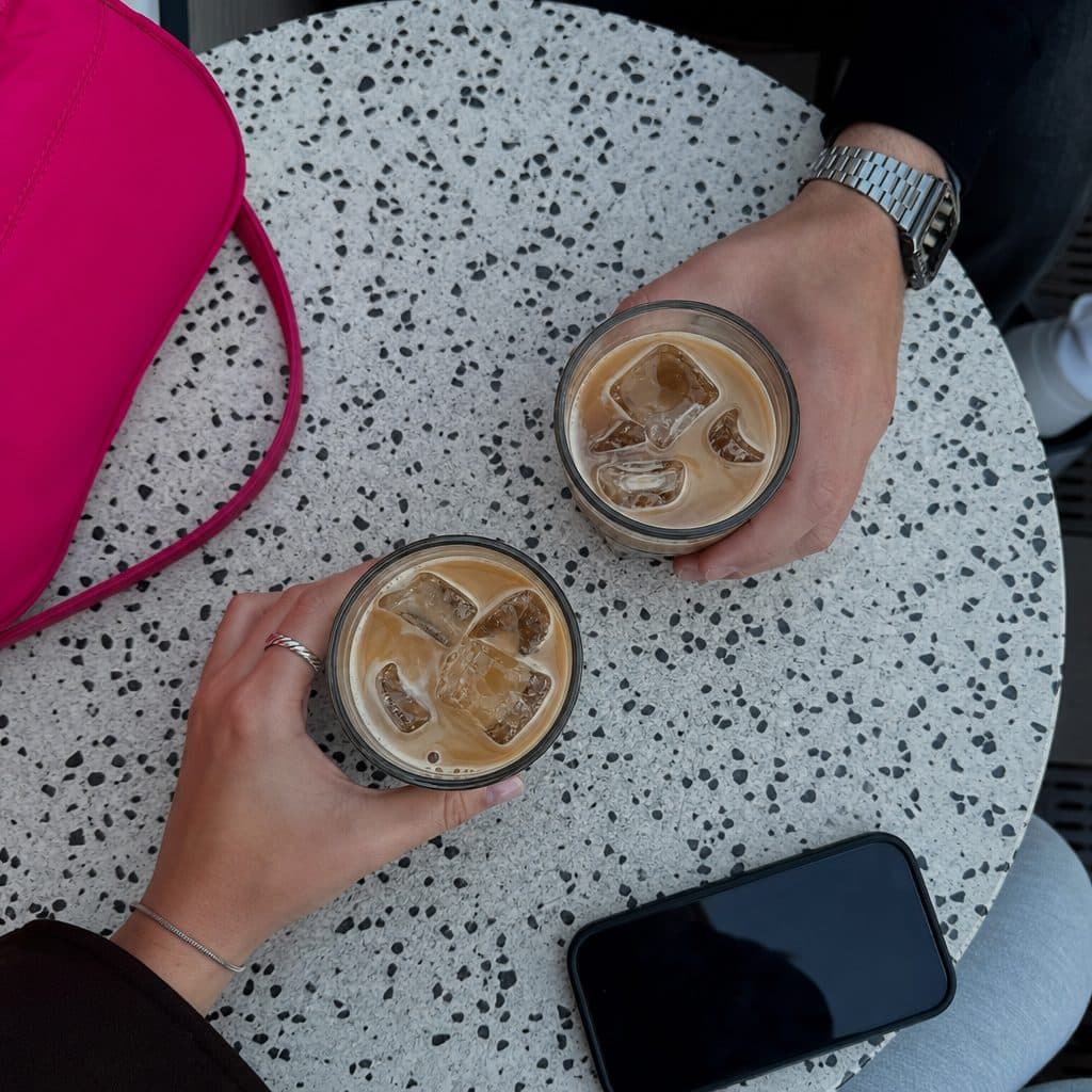 Zwei Hände mit Eiskaffee über einem Terrazzo-Tisch