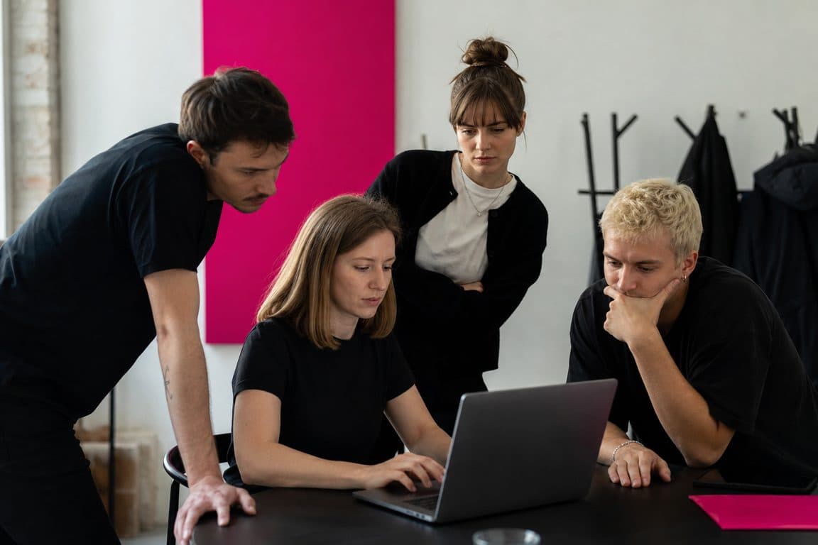 Team steht ernst um einen Laptop, eine Person tippt eine Antwort
