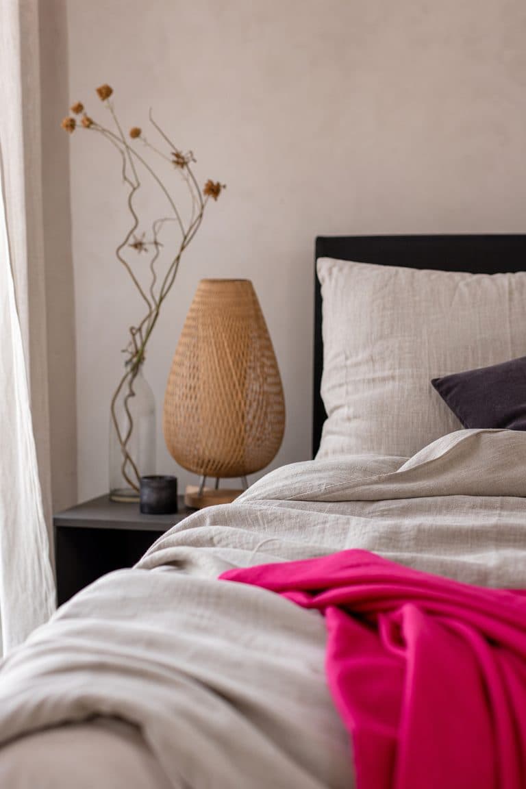 Schlafzimmerecke mit Leinenbettwäsche und Rattanlampe