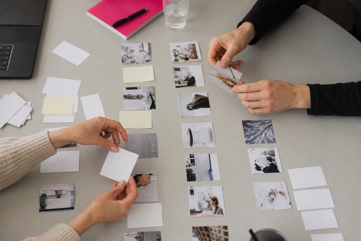 Hände ordnen ausgedruckte Beiträge und Notizzettel auf einem Workshop-Tisch zu Spalten