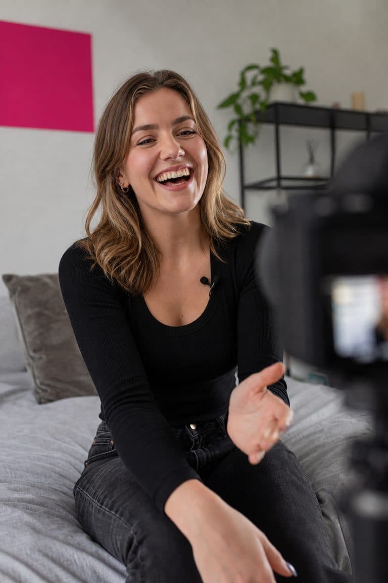 Junge Frau lacht beim Aufnehmen eines Videos mit Ansteckmikrofon